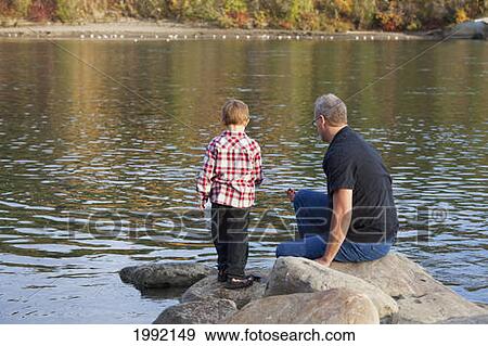 Stock Photo - Grandfather And Grandson Playing Along The Rocks At The River's Edge; Edmonton Alberta Canada. Fotosearch