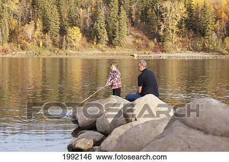Stock Photograph - Grandfather And Grandson Playing Along The Rocks At The River's Edge; Edmonton Alberta Canada. Fotosearch