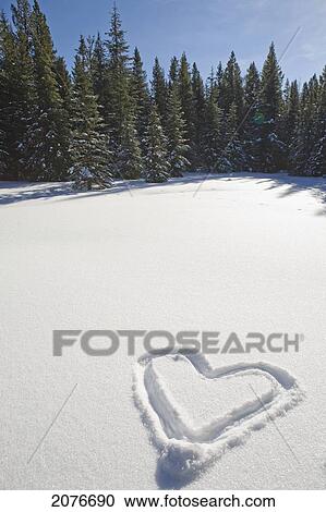 Stock Image - Heart shape drawn in snow covered meadow with evergreen trees in background and blue sky; lake louise alberta canada. Fotosearch