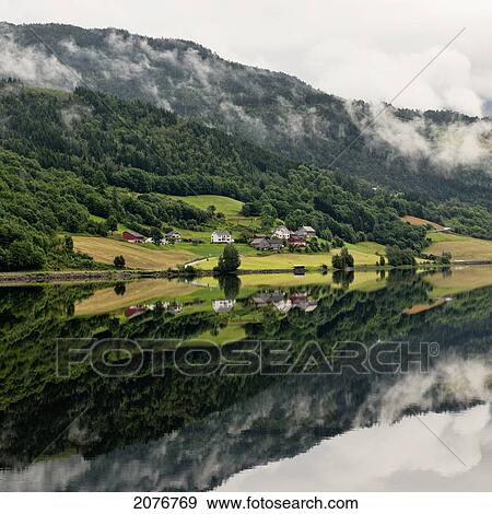 Stock Photo - Houses and a forest on a mountainside reflected in tranquil water; granvin norway. Fotosearch