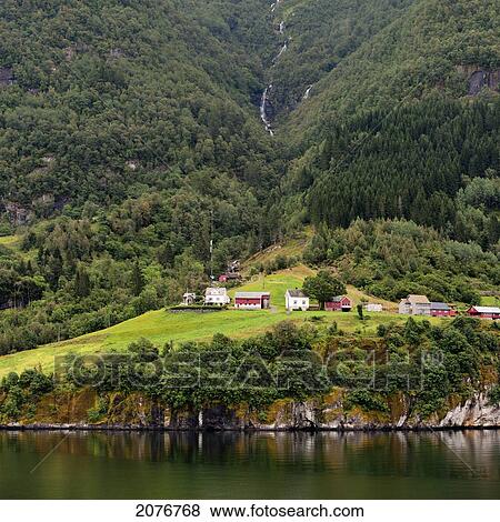 Houses at the base of a tree covered mountain along the water's edge; granvin norway View Large Photo Image Stock Photo - Houses at the base of a tree covered mountain along the water's edge; granvin norway. Fotosearch