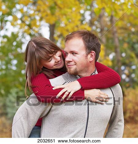 Stock Image - Husband Carrying His Wife On His Back In A Park In Autumn; Edmonton Alberta Canada. Fotosearch