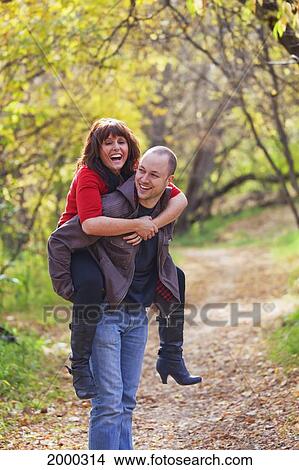 Husband Carrying His Wife Piggy Back In A Park In Autumn; Edmonton Alberta Canada View Large Photo Image Picture - Husband Carrying His Wife Piggy Back In A Park In Autumn; Edmonton Alberta Canada. Fotosearch