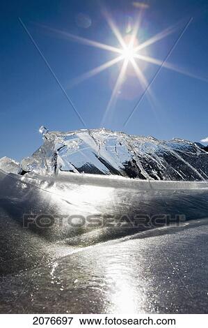 Ice formations on a frozen lake shoreline in the mountains with a sunburst and blue sky; alberta canada View Large Photo Image Stock Photo - Ice formations on a frozen lake shoreline in the mountains with a sunburst and blue sky; alberta canada. Fotosearch