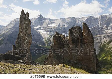 Stock Photo - Large Rock Sentinels On Mountain Ridge With A Mountain Range In The Distance With Blue Sky And Clouds; Alberta Canada. Fotosearch