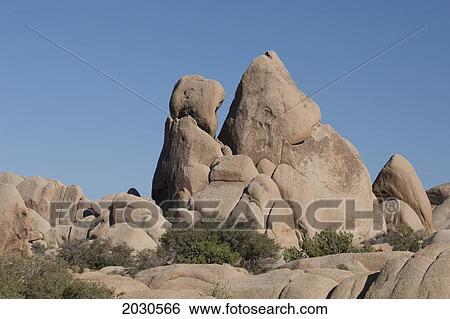 Stock Photograph - Large Rounded Rock Formation In The Desert With Shurbs And Blue Sky; Palm Springs California United States Of America. Fotosearch
