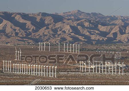 Stock Image - Large Windmill Farm In A Desert Valley With Desert Mountain Range In The Distance At Sun Set And Blue Sky; Palm Springs California United States Of America. Fotosearch