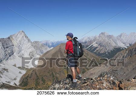 Stock Photograph - Male Hiker On Top Of Mountain Ridge Overlooking Valley And Mountains In The Distance With Blue Sky; Alberta Canada. Fotosearch