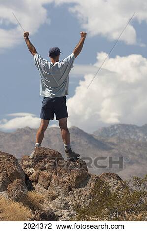 Male Hiker With Arms Raised On Top Of A Desert Mountain With Mountain Range In Distance; Palm Springs California United States Of America View Large Photo Image Stock Image - Male Hiker With Arms Raised On Top Of A Desert Mountain With Mountain Range In Distance; Palm Springs California United States Of America. Fotosearch