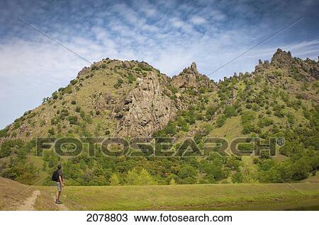 Stock Image - Man with backpack looking up at sky and mountains; sutter buttes california united states of america. Fotosearch