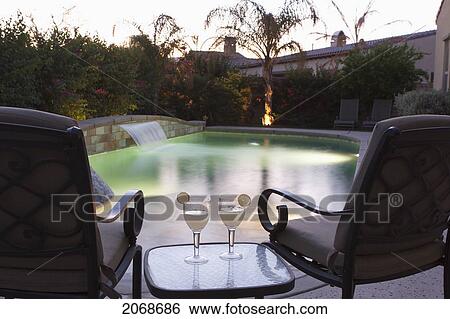 Stock Photograph - Pool Side Setting At Dusk With Pool Lights Two Chairs Table And Two Glasses With Lime Wedges; Palm Springs California United States Of America. Fotosearch