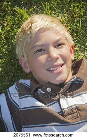 Stock Image - Portait Of A Boy With Blond Hair Laying On The Grass; Moraga California United States Of America. Fotosearch