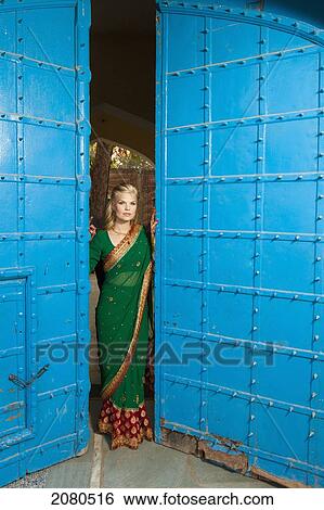 Stock Photograph - Portrait of a blond woman wearing a sari standing in the doorway with large blue doors; ludhiana punjab india. Fotosearch