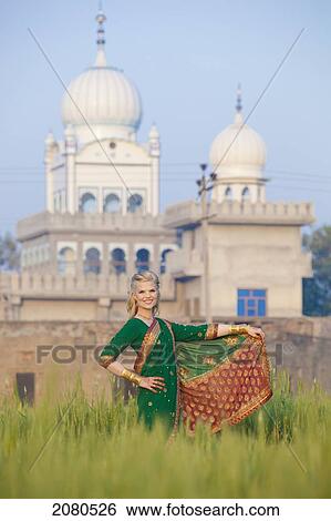 Stock Photograph - Portrait of a blond woman wearing a sari in a field with a temple in the background; ludhiana punjab india. Fotosearch