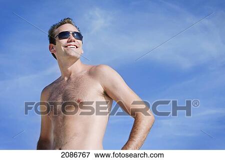 Portrait of a man wearing a swimsuit and sunglasses against a blue sky; punta cana la altagracia dominican republic View Large Photo Image Stock Photo - Portrait of a man wearing a swimsuit and sunglasses against a blue sky; punta cana la altagracia dominican republic. Fotosearch