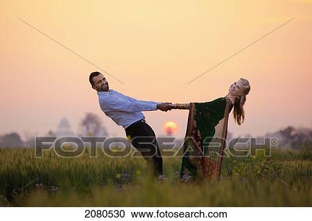 Stock Image - Portrait of a mixed race couple her wearing a sari in a field at sunset; ludhiana punjab india. Fotosearch