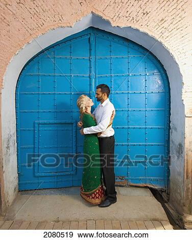 Stock Photo - Portrait of a mixed race couple with her wearing a sari standing in the doorway with large blue doors; ludhiana punjab india. Fotosearch