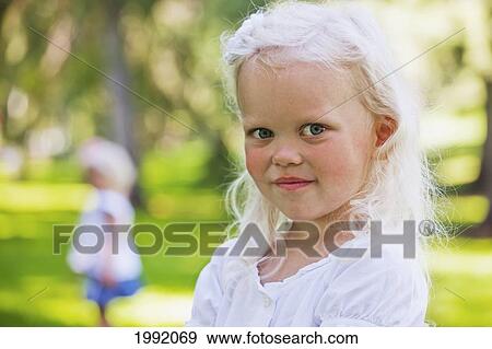 Portrait Of A Young Girl In The Park With Her Sister In The Background; Edmonton Alberta Canada View Large Photo Image Stock Photo - Portrait Of A Young Girl In The Park With Her Sister In The Background; Edmonton Alberta Canada. Fotosearch