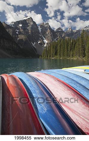 Row Of Canoes On Their Sides With A Lake Mountains Clouds And Blue Sky; Alberta Canada View Large Photo Image Stock Photography - Row Of Canoes On Their Sides With A Lake Mountains Clouds And Blue Sky; Alberta Canada. Fotosearch
