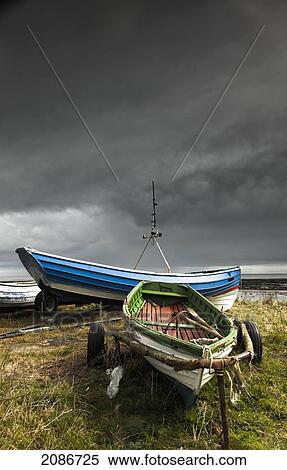 Rowboats sitting on trailers on the shore under storm clouds; boulmer northumberland england View Large Photo Image Stock Photography - Rowboats sitting on trailers on the shore under storm clouds; boulmer northumberland england. Fotosearch