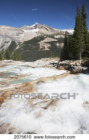 Rushing Mountain River With Mountain Range In The Distance And Blue Sky; Field British Columbia Canada View Large Photo Image Stock Image - Rushing Mountain River With Mountain Range In The Distance And Blue Sky; Field British Columbia Canada. Fotosearch