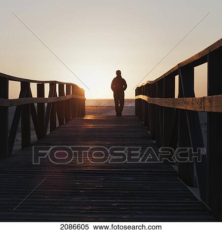 Silhouette of a person walking on a wooden boardwalk towards the beach and ocean; tarifa cadiz andalusia spain View Large Photo Image Stock Photography - Silhouette of a person walking on a wooden boardwalk towards the beach and ocean; tarifa cadiz andalusia spain. Fotosearch