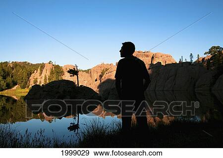 Stock Photo - Silhouette Of A Young Man Standing At The Water's Edge Of Sylvan Lake; Black Hills South Dakota United States Of America. Fotosearch