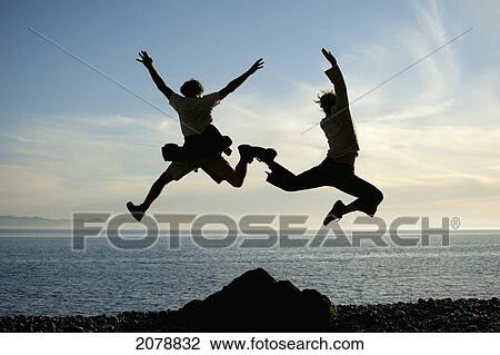 Silhouette of two people leaping in the air at the water's edge; vancouver island british columbia canada View Large Photo Image Stock Image - Silhouette of two people leaping in the air at the water's edge; vancouver island british columbia canada. Fotosearch