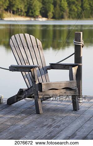 Stock Image - Single deck chair on wooden deck on a lake; flesherton ontario canada. Fotosearch