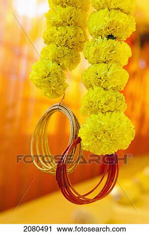 Stock Image - Strings of yellow flowers with gold and red bracelets dangling from the bottom; ludhiana punjab india. Fotosearch