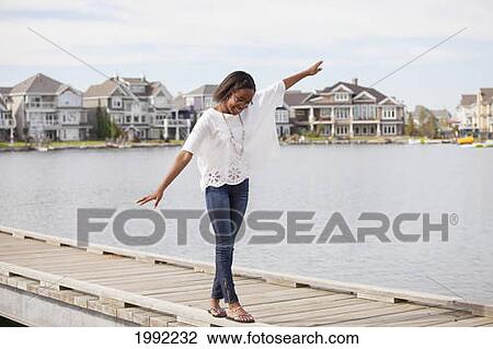 Stock Image - Teenage Girl Balancing On The Rail Of A Pier In A Residential Lake Neighborhood; Edmonton Alberta Canada. Fotosearch