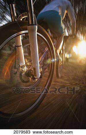Stock Image - The motion of a bicycle wheel as a cyclist rides on a path at sunset; tarifa cadiz andalusia spain. Fotosearch