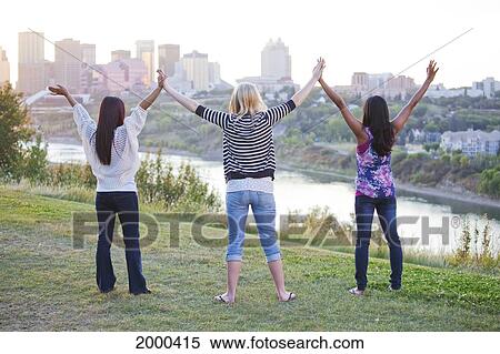 Stock Photography - Three Girls Raising Their Hands Together With The City Skyline In The Background; Edmonton Alberta Canada. Fotosearch