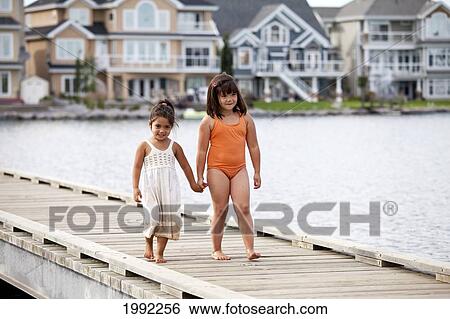 Stock Photograph - Two Sisters On A Pier At A Residential Lake Area; Edmonton Alberta Canada. Fotosearch