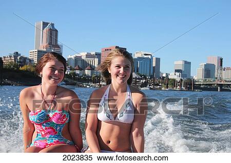 Stock Photography - Two Teenage Girls Sitting On The Back Of A Boat With The City Of Portland In The Background; Portland Oregon United States Of America. Fotosearch