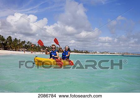 Picture - Two women in lifejackets paddling in a yellow boat; punta cana la altagracia dominican republic. Fotosearch