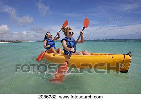 Stock Image - Two women in lifejackets paddling in a yellow boat; punta cana la altagracia dominican republic. Fotosearch