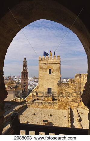 Stock Image - View through arabic horseshoe shaped arch across patio of the cisterns to the keep of the alcazar with church of san pedro behind; carmona seville province spain. Fotosearch