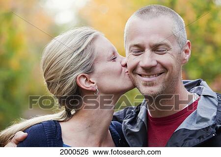 Stock Photograph - Wife Kissing Husband On The Cheek In A Park In Autumn; Edmonton Alberta Canada. Fotosearch