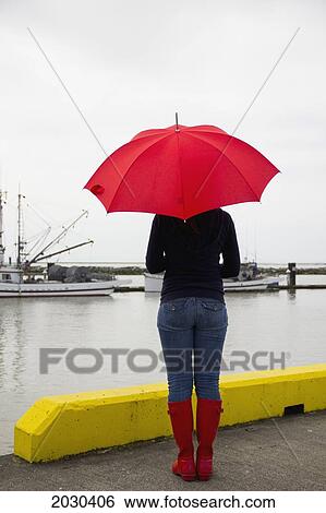 Stock Photograph - Woman On A Pier With A Red Umbrella And Rain Boots; Richmond British Columbia Canada. Fotosearch