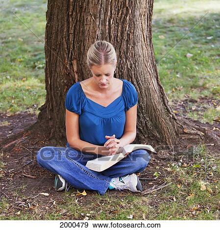 Stock Photo - Woman Reading Her Bible And Praying In The Park Beside A Tree; Edmonton Alberta Canada. Fotosearch
