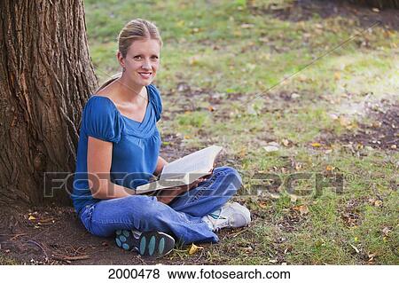 Stock Photo - Woman Reading Her Bible In The Park Beside A Tree; Edmonton Alberta Canada. Fotosearch