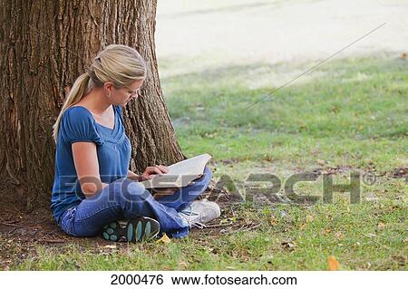 Stock Photograph - Woman Reading Her Bible In The Park Beside A Tree; Edmonton Alberta Canada. Fotosearch