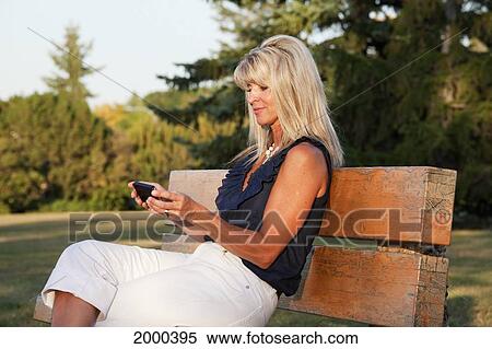 Woman Relaxing On A Park Bench At Dusk Reading Text Messages On Her Phone; Edmonton Alberta Canada View Large Photo Image Stock Photography - Woman Relaxing On A Park Bench At Dusk Reading Text Messages On Her Phone; Edmonton Alberta Canada. Fotosearch