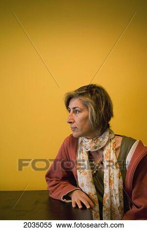 Woman Sitting At A Table Against An Orange Wall Looking Sideways; Calgary Alberta Canada View Large Photo Image Stock Photography - Woman Sitting At A Table Against An Orange Wall Looking Sideways; Calgary Alberta Canada. Fotosearch