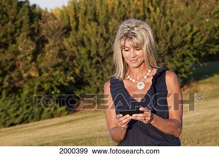 Stock Photo - Woman Walking In The Park At Dusk Reading Text Messages; Edmonton Alberta Canada. Fotosearch