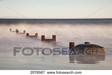 Stock Photo - Wooden posts and boulders immersed in water at the coast; northumberland england. Fotosearch