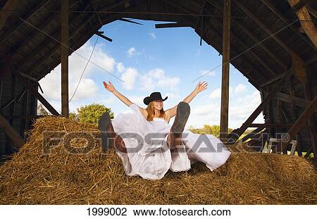 Stock Image - Young Bride Smiling In A Barn With Cowgirl Hat And Boots; Pennock Minnesota United States Of America. Fotosearch
