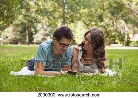 Stock Image - Young Couple Looking At Text Messages Together In The Park; Edmonton Alberta Canada. Fotosearch