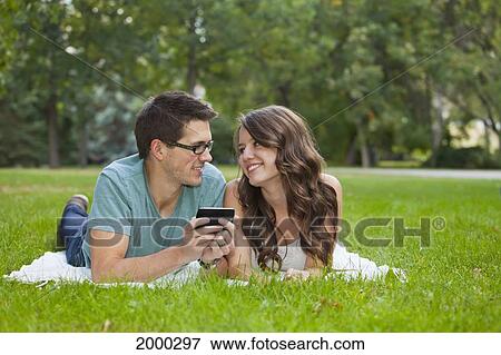 Stock Photo - Young Couple Looking At Text Messages Together In The Park; Edmonton Alberta Canada. Fotosearch